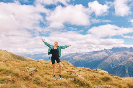 Outdoor portrait of happy young woman hiking in autumn mountains, arms wide openの写真素材