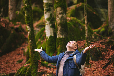 Handsome middle age man hiking in forest, wearing warm jacket, backpack and glassesの写真素材