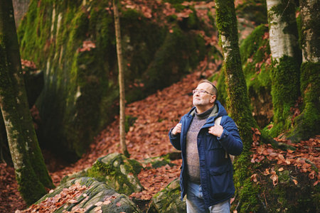 Handsome middle age man hiking in forest, wearing warm jacket, backpack and glassesの写真素材