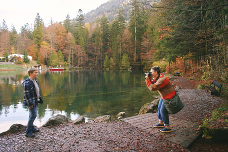 Young happy woman taking picture of preteen kid by mountain lake, family travel with childrenの写真素材