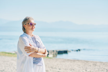 Outdoor summer portrait of happy and healthy mature 50 - 55 year old woman enjoying nice sunny day by the lake or sea, active lifestyleの写真素材