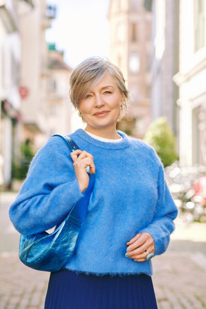 Outdoor portrait of beautiful middle age 55 - 60 year old woman posing outside, wearing blue pulloverの写真素材