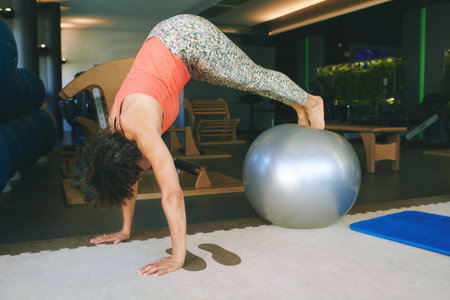 Portrait of mature 50 - 55 year old woman training with fitness ball at gym, healthy lifestyle