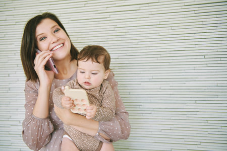 Happy young mother talking on the phone, holding little baby playing with silicone toy phoneの写真素材