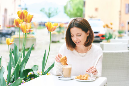 Portrait of happy mature woman having coffee with croissant in outdoor cafeの写真素材