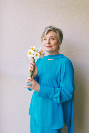 Portrait of beautiful 55 - 60 year old woman with gray hair, holding bouquet of daffodil flowersの写真素材