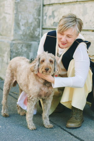 Outdoor portrait of happy mature woman petting labradoodle dogの写真素材