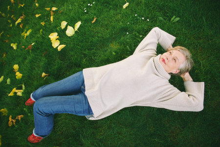 Outdoor portrait of happy mature woman laying on green grass, wearing warm pullover or sweater. Active and healthy lifestyle. Top view, flat layの写真素材