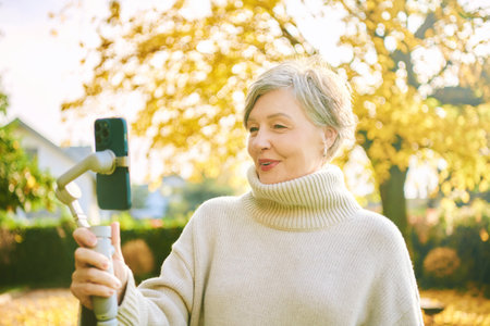 Outdoor portrait of happy and active mature woman recording herself with phone, social media and vlogging conceptの写真素材