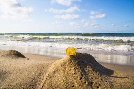 Amber in the sand against the background of sea waves and skyの写真素材