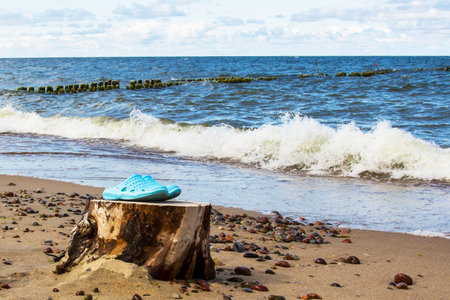 Slippers by the sea with legs Blue beach sandals at the water's edge on the sandの写真素材