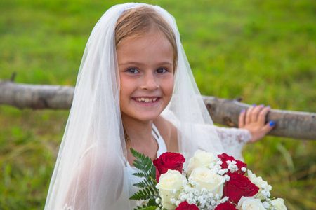 Children's day. the little girl in a bride's dress  a veil and a wedding bouquetの写真素材