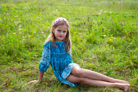 portrait of a cute little girl lying in a meadow. Beautiful girl with curly blonde hair in a dress and bare feetの写真素材