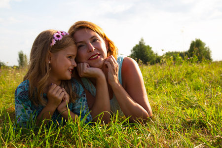 a little girl and a woman-mother lie on the green grass in a field,, a child's smile and joy, a daughter tells her children's secretsの写真素材