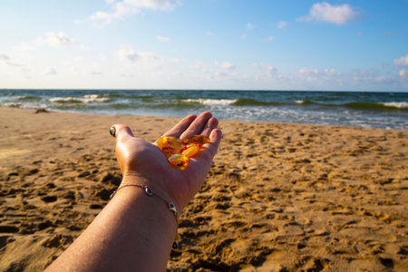 Amber in the palm of your hand. A group of pieces of transparent mineral Sunstone on a woman's hand against the background of the sea and sand. Semi-precious stones. The Baltic seaの写真素材