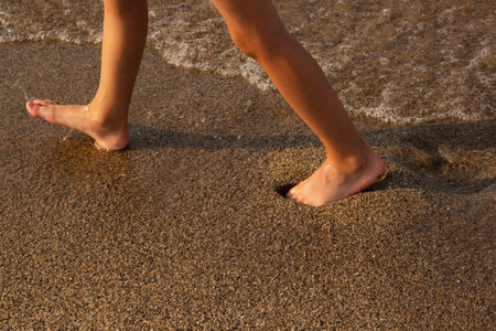Beach trip-a woman walks on a sandy beach, leaving footprints in the sand. Close-up details of women's legs and Golden sand on the beachの写真素材