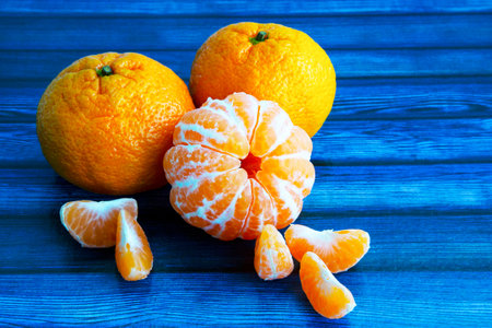 on a blue wooden table. Tangerines in the skin and without the skin. Slices of peeled tangerine. Citrus fruitsの写真素材