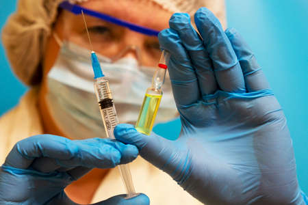 Doctor with a syringe and ampoule, close-up. Vaccination and immunization. A female doctor wearing a...