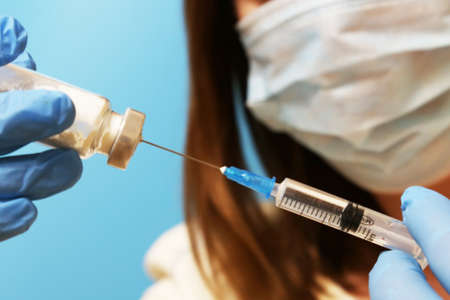 Doctor filling syringe with medication, closeup. Vaccination and immunization. A female doctor wearing a mask and gloves with an ampoule and a syringe oの写真素材