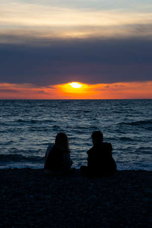 Couple in love watching sunset together on beach travel summer holidays. People silhouette from behind sitting enjoying view sunset sea on tropical destination vacation. Romantic couple on the beachの写真素材