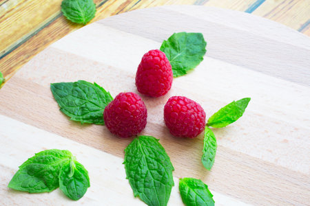Fresh raspberries and mint on a wooden table. Ripe red raspberries and green peppermint leaves on a...