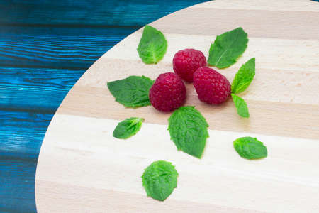 Fresh raspberries and mint on a wooden table. Ripe red raspberries and green peppermint leaves on a wooden standの写真素材
