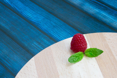 Fresh raspberries and mint on a wooden table. Ripe red raspberries and green peppermint leaves on a...