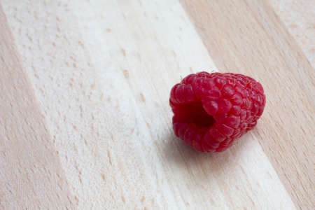 Fresh raspberries lay on the wooden table in close-up. Ripe red raspberries, healthy fruits on a wooden textured table in detail. Small juicy berries.の写真素材