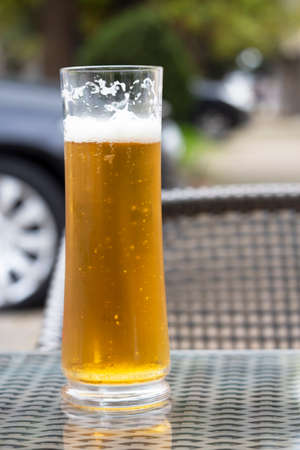 Beer with a glass mug on a wooden table on the terrace of an outdoor cafe. In the background is a...