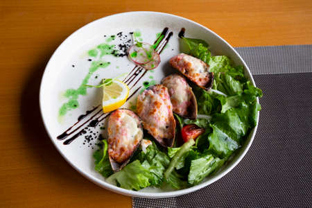 seafood baked in cream sauce and mussel cheese with vegetables on a white plate in a fish restaurantの写真素材