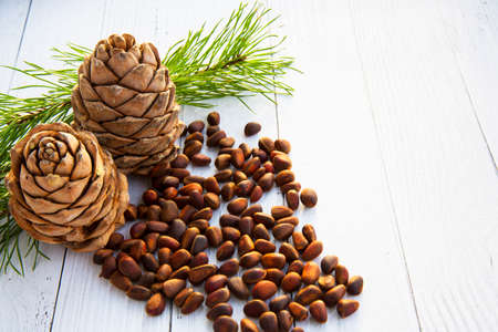 Peeled kernels of cedar nuts in a spoon, two pine cones, green branches and nuts in the shell against a dark wooden boardの写真素材