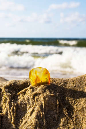 Amber in the sand against the background of sea waves and blue skyの写真素材