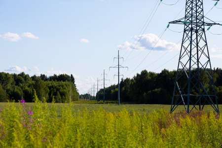 High voltage pylons at spring summer countryside, forest and blue sky with cloudsの写真素材