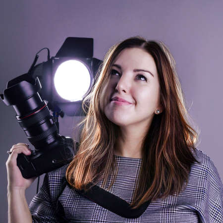 A female photographer in a studio with a SLR camera and lighting equipment looks up dreamilyの写真素材