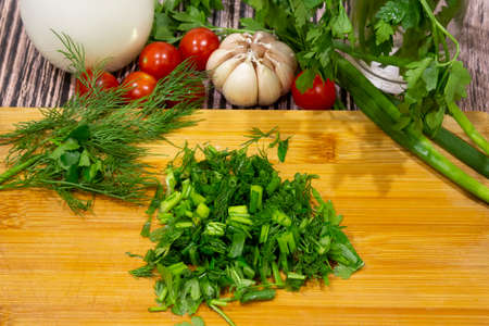 Bunches of green onions, parsley and dill on a wooden chopping board next to tomatoes, potatoes,...