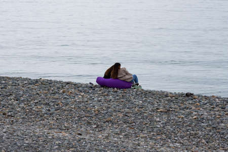 Two friends are sitting in bag chairs and looking at the sea. Bean bag chair on the beach, early springの写真素材