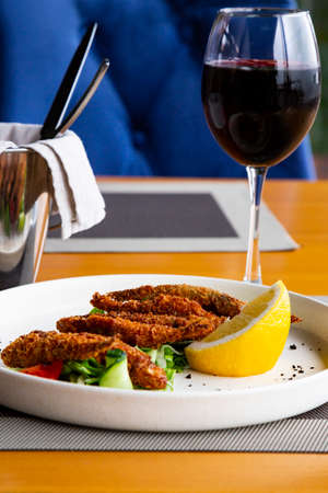 Fried smelt with lemon and vegetables on the table with a glass of red wine. A small fish. Mediterranean cuisineの写真素材