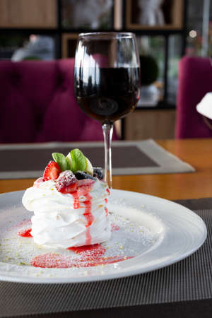Pavlov dessert with whipped whites and berries and a glass of red wine in the restaurant.