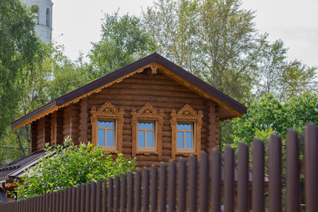 There is a timber cottage behind the fence. A wooden house behind a brick wall n summerの写真素材