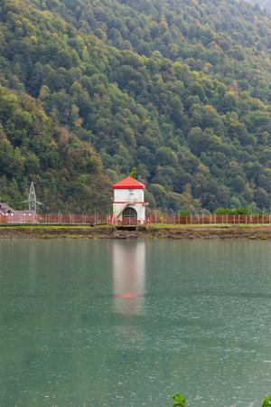 A white building with a red roof on the shore of a lake on a rainy day, autumn.の写真素材