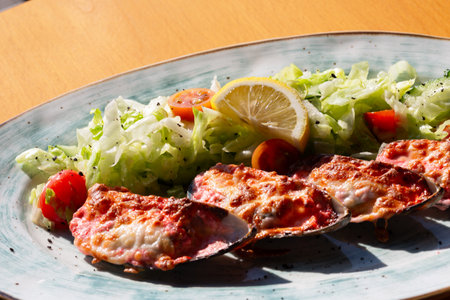 baked mussels with cheese on a white plate with lemonの写真素材