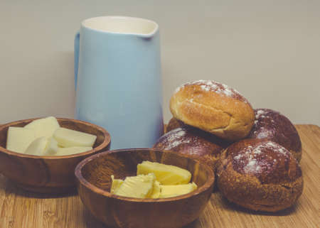Simple rustic breakfast with bread buns butter and milk on a wooden board.の写真素材