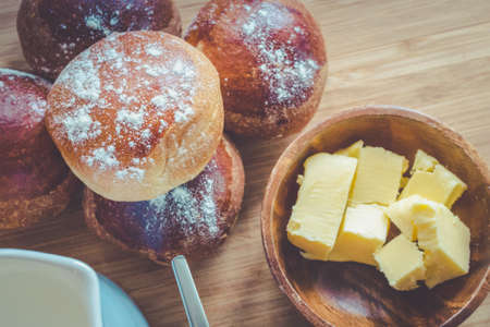 Simple rustic breakfast with bread buns butter and milk on a wooden board.の写真素材
