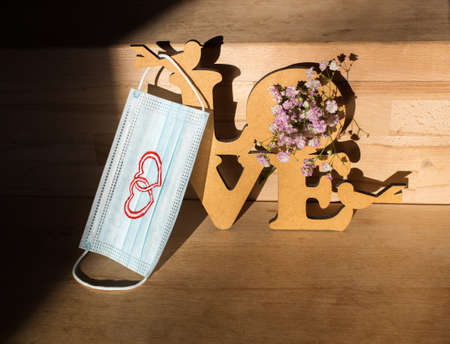 Valentine's Day celebration concept. medical protective mask with drawn hearts, wooden inscription...