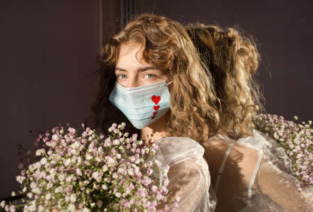 portrait of cute teenage girl in a medical mask with red hearts painted on it, with a bunch of...