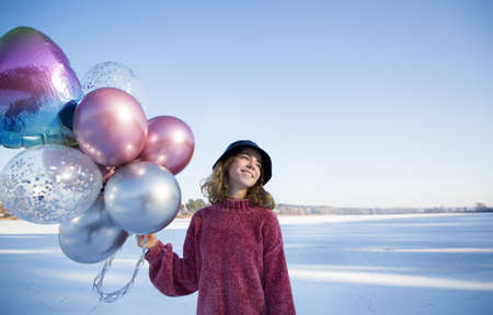 Portrait of tender happy teenage girl in pink sweater, panama hat holding many colorful balloons in hands. sunny winter day. feels great, festive, enjoys moment. Birthday girl, surprise from loved oneの写真素材