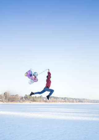 graceful slender pretty teenage girl, holding many colorful balloons in her hands, jumping over the snowy ground. sunny winter holiday. Joyful emotions, life energy, no problemsの写真素材