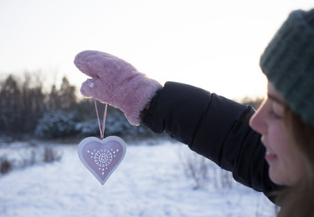 Valentine's day background. hand in fluffy pink mitten holds decorative ornament against background of snowy forest. Smiling face of young woman out of focus. Holiday and relationship conceptの写真素材