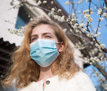 Young beautiful woman in a medical face mask outdoors near a blossoming tree. Wear masks to prevent . Real life during the  pandemicの写真素材