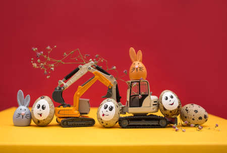 models of toy excavators, Easter bunnies, Easter quail eggs with painted smiles and eyes. Congratulations concept for business building companies. postcard. copy spaceの写真素材
